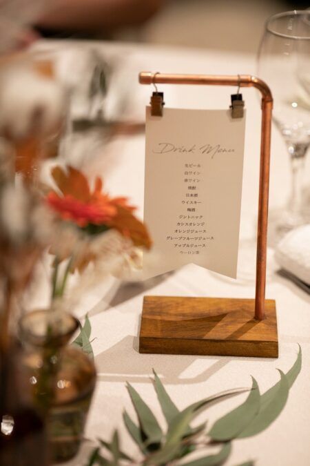 a place card holder on top of a wooden stand at a table with white linens and greenery