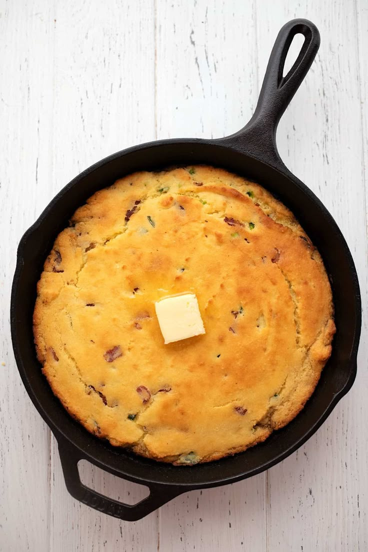 a skillet with some food in it on top of a white wooden table next to a piece of butter