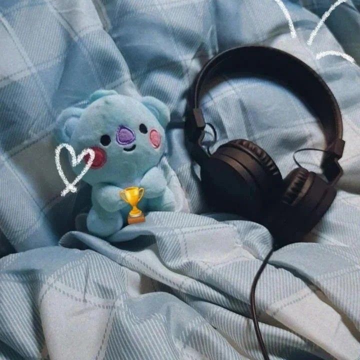 a blue teddy bear with headphones laying on a bed next to a pair of headphones