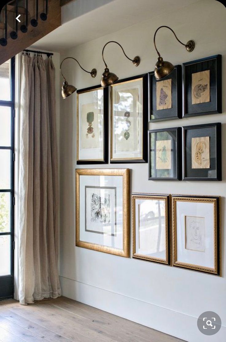 several framed pictures hang on the wall next to a window in a room with wooden floors