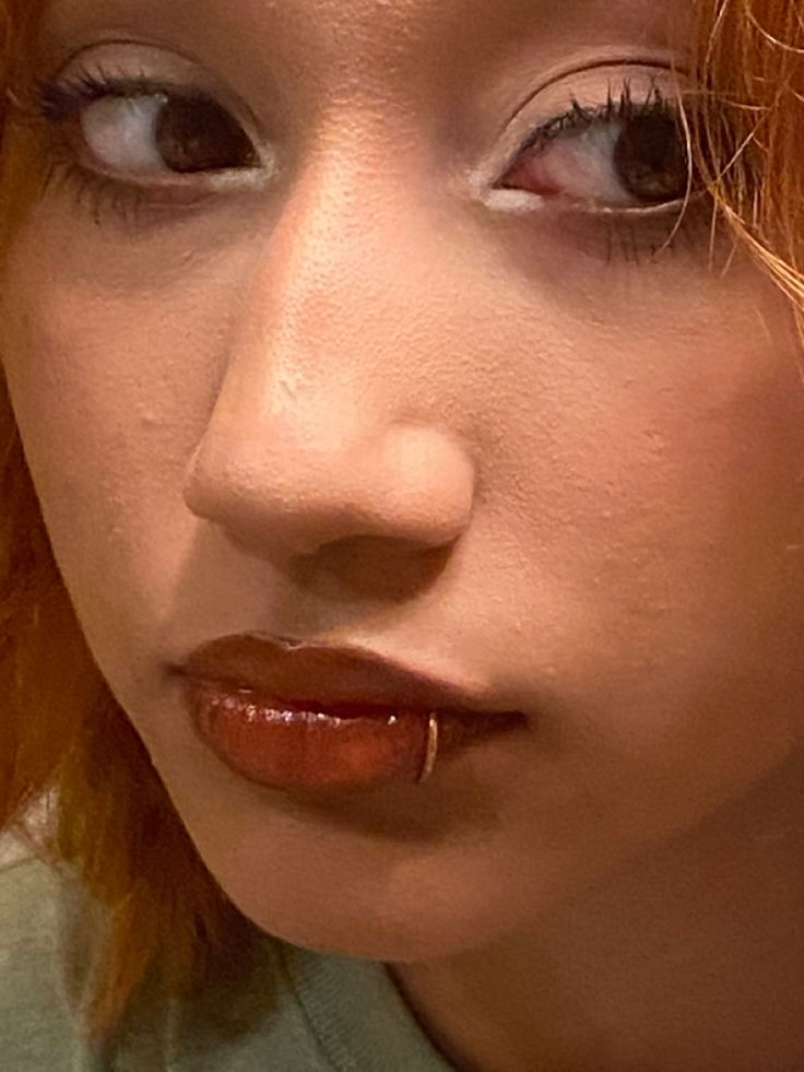 a close up of a person with red hair and piercings on her nose looking at the camera