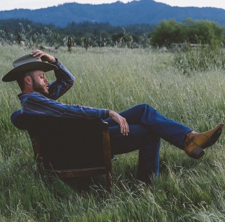 a man with a cowboy hat sitting on a chair in tall grass looking at the sky