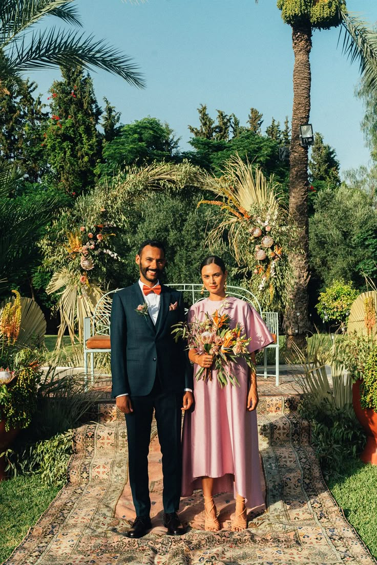 a man and woman standing next to each other in front of palm trees on a rug