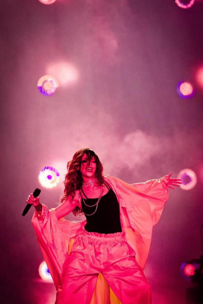 a woman in pink and yellow outfit on stage with lights behind her holding a microphone