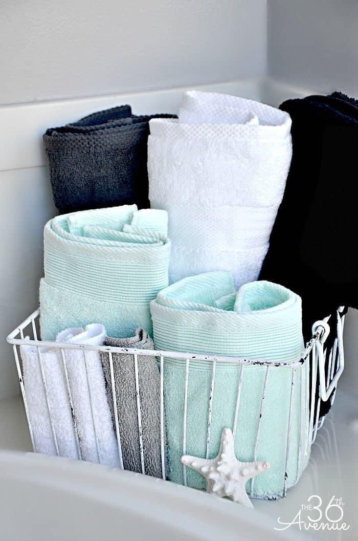 towels and other bathroom items are in a metal basket on the sink's edge