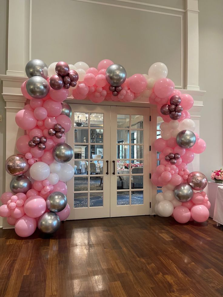 a large balloon arch is decorated with pink, silver and white balloons