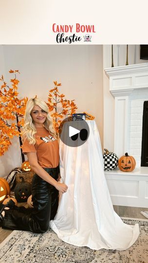 a woman standing next to a fake ghost in a living room with pumpkins on the floor