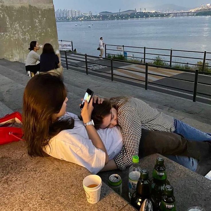 two people laying on the ground next to each other with beer bottles and water in the background