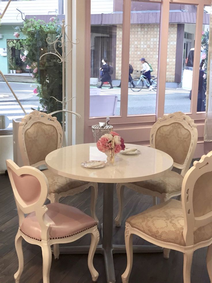 a white table with four chairs and a vase on it in front of a window