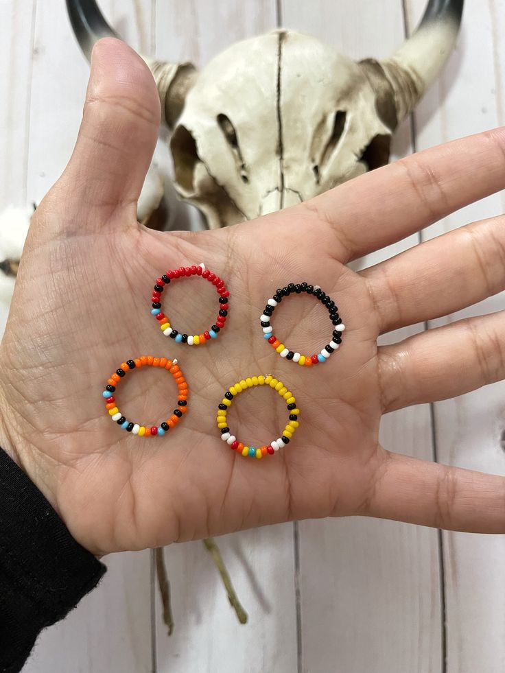 the hand is holding three small beaded bracelets in front of a cow skull