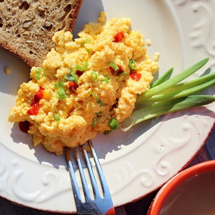 an egg salad on a plate with a fork and cup of tea next to it