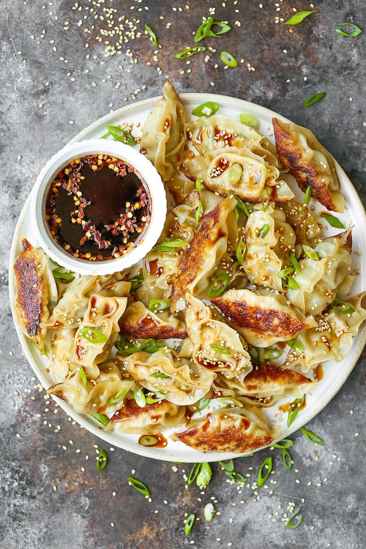 a white plate topped with dumplings covered in sauce and sprinkled with sesame seeds