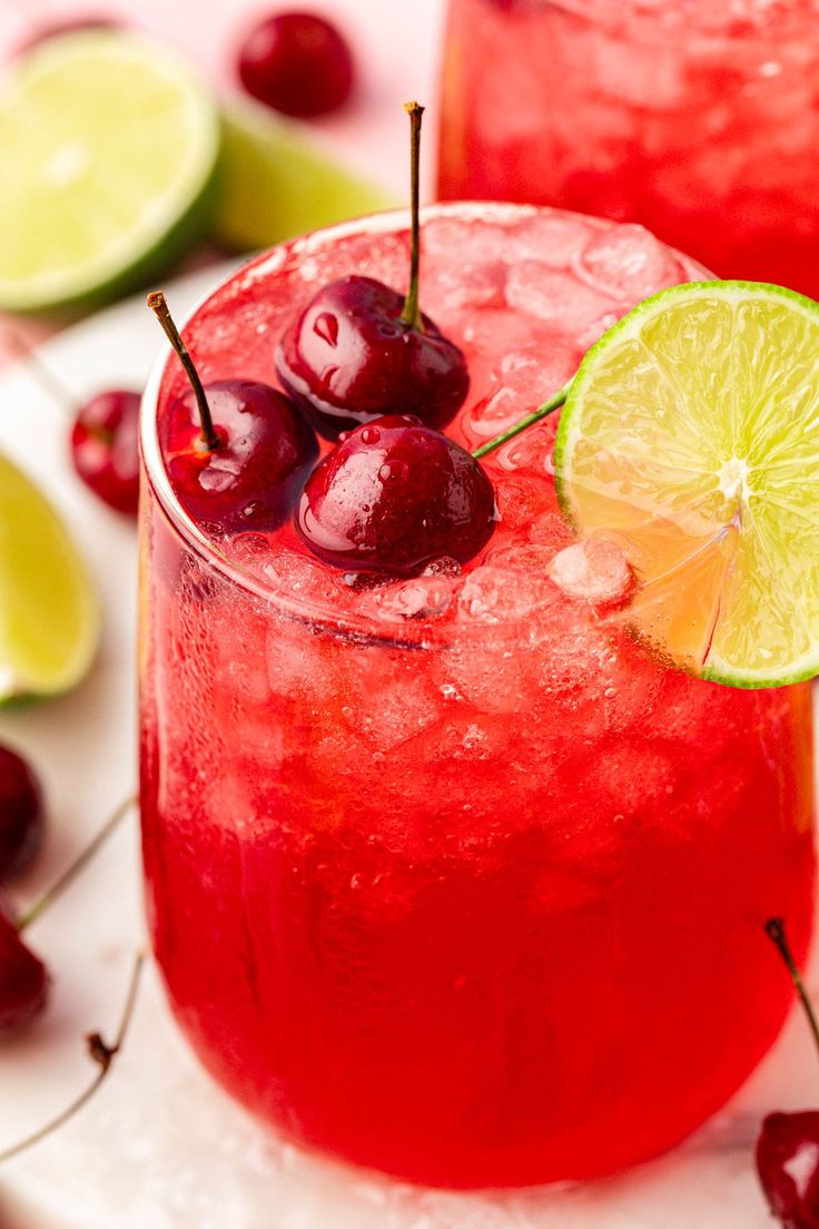 two cocktails with cherries and lime on the rim, sitting next to each other