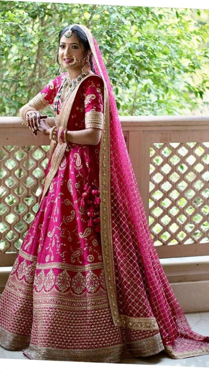 a woman in a red and gold bridal gown standing on a balcony with trees behind her