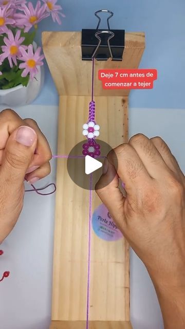 two hands are making beaded bracelets on a piece of wood with pink and white beads