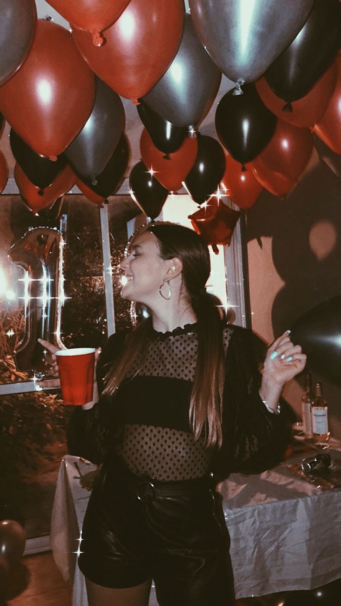 a woman standing in front of balloons with her mouth open and holding a drink up to the ceiling