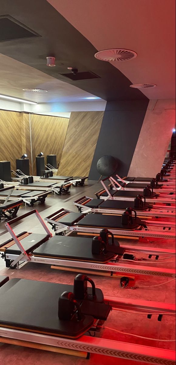 rows of treadmills lined up on the floor in an empty room with red lighting