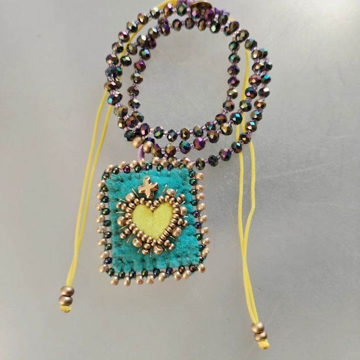 the beaded necklace has a heart on it and is attached to a yellow cord