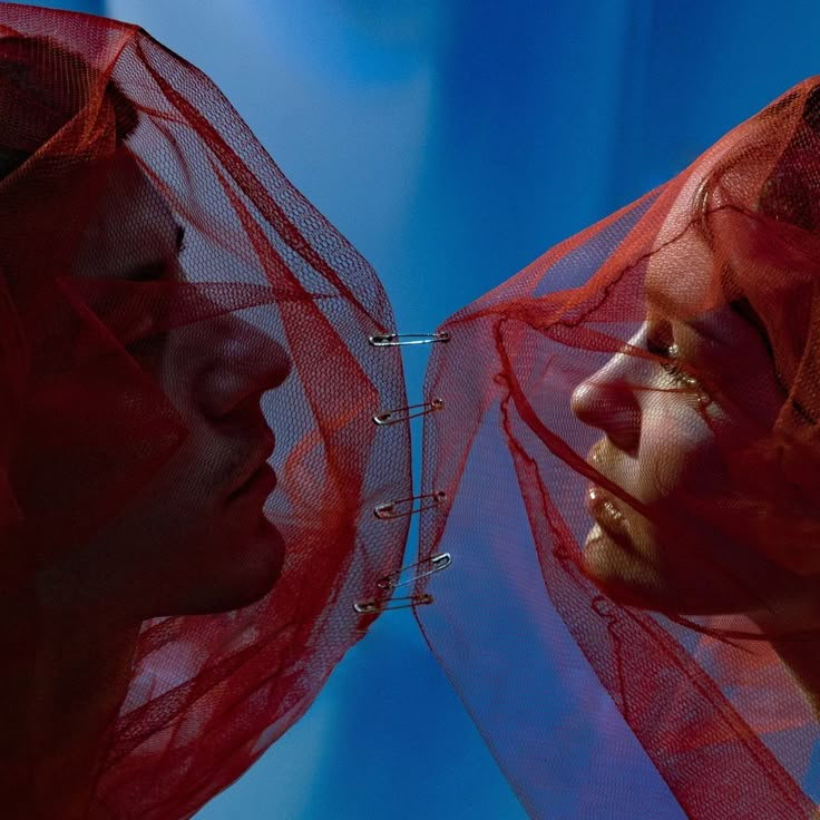 two women with red veils on their heads looking into each other's eyes