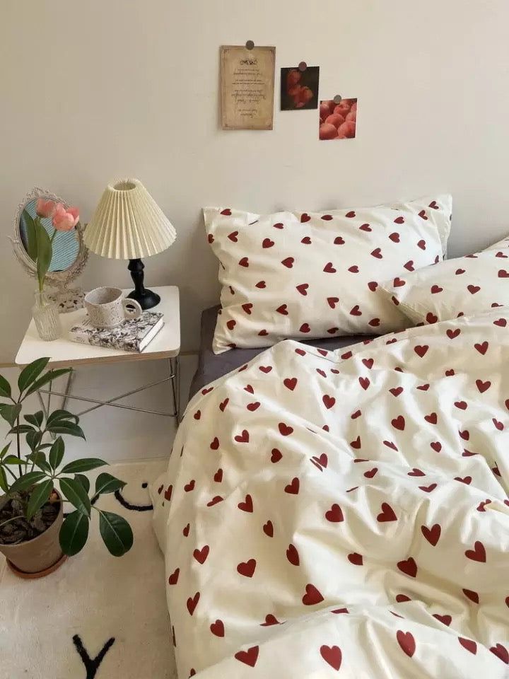 a bed with white sheets and red hearts on it, next to a small table