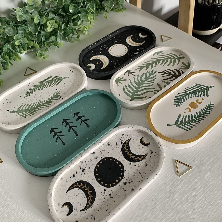 four ceramic trays with designs on them sitting on a table next to a potted plant