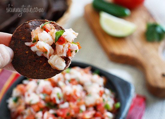 a person is holding up a tortilla with shrimp and salsa on it in front of a cutting board