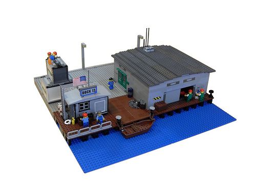 a lego model of a boat dock with people on it and a building in the background