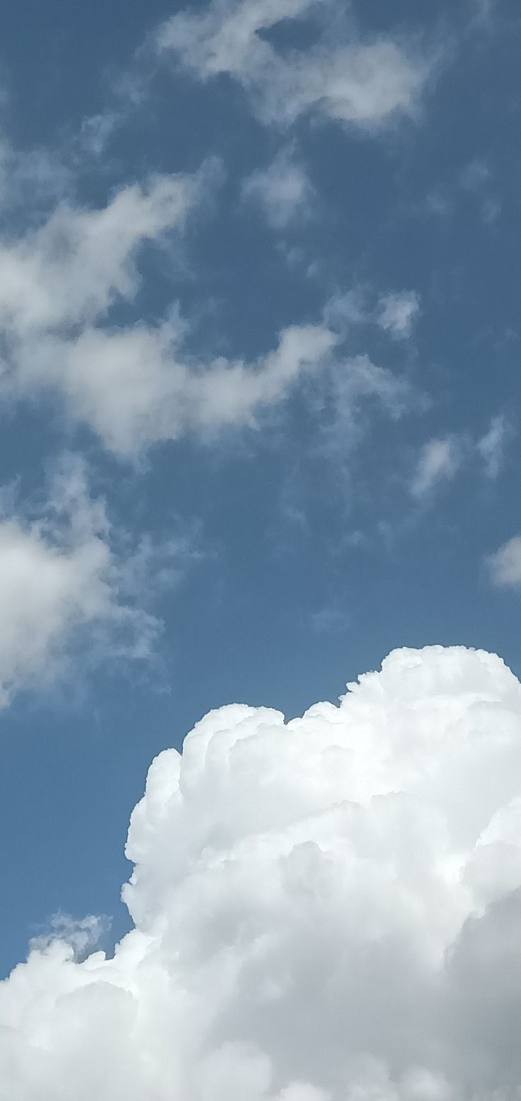 the plane is flying high in the blue sky with fluffy white clouds behind it,