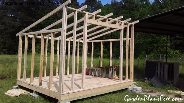 a house being built in the middle of a field with trees and grass behind it