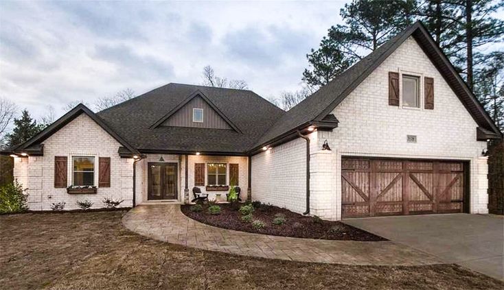 a white brick house with brown shutters on the front and garage doors open to let in light