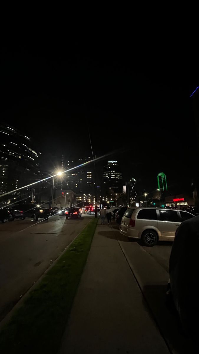 cars are parked on the side of the road at night with city lights in the background