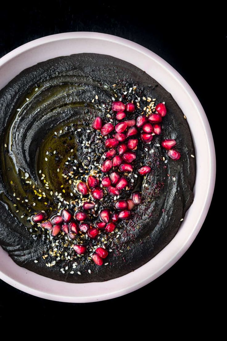 a white bowl filled with black hummus and pomegranates on top