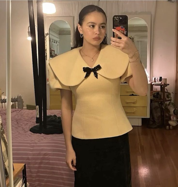 a woman taking a selfie in front of a mirror wearing a bow tie top