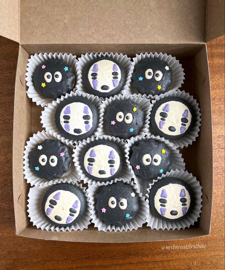 some cupcakes are in a box on a wooden table and have faces painted on them