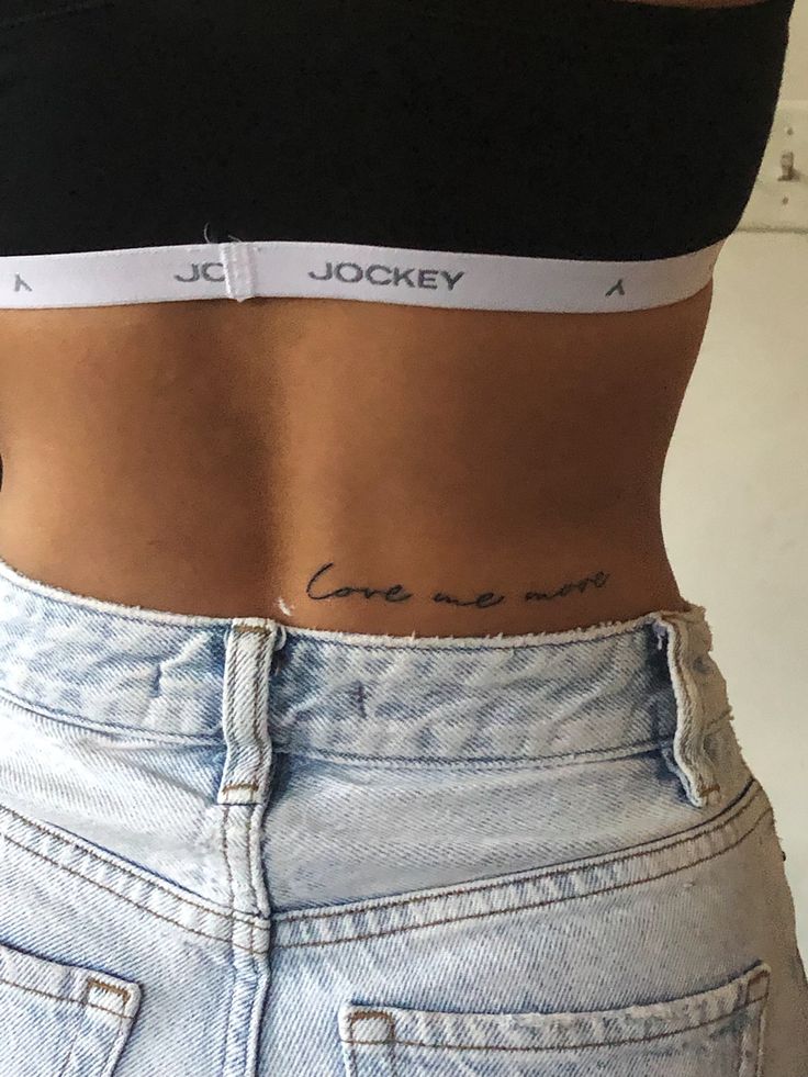 Back script tattoo reading, “love me more” Waist Back Tattoos For Women, One Worded Tattoos, Tattoo Ideas Waist For Women, Lower Back Writing Tattoo, Lower Back Quote Tattoo, Back Tattoo Phrase, Lower Back Script Tattoos, Lower Back Small Tattoos, Back Script Tattoo Women