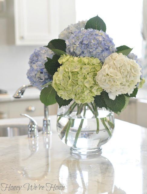 a vase filled with blue and white flowers on top of a kitchen counter next to a sink