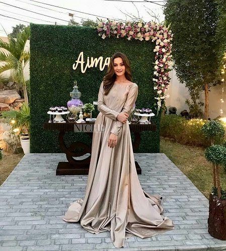 a woman standing in front of a sign wearing a long dress with sleeves on it