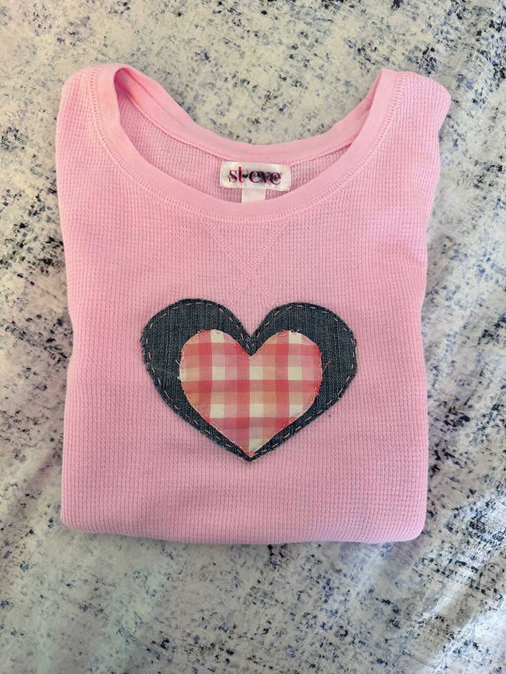 a pink sweater with a black heart on the front and plaid patch in the back