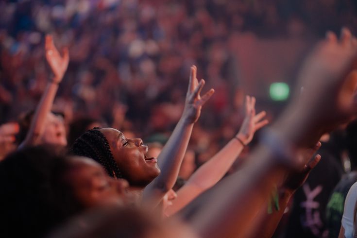 a group of people at a concert with their hands in the air and one person holding up her hand