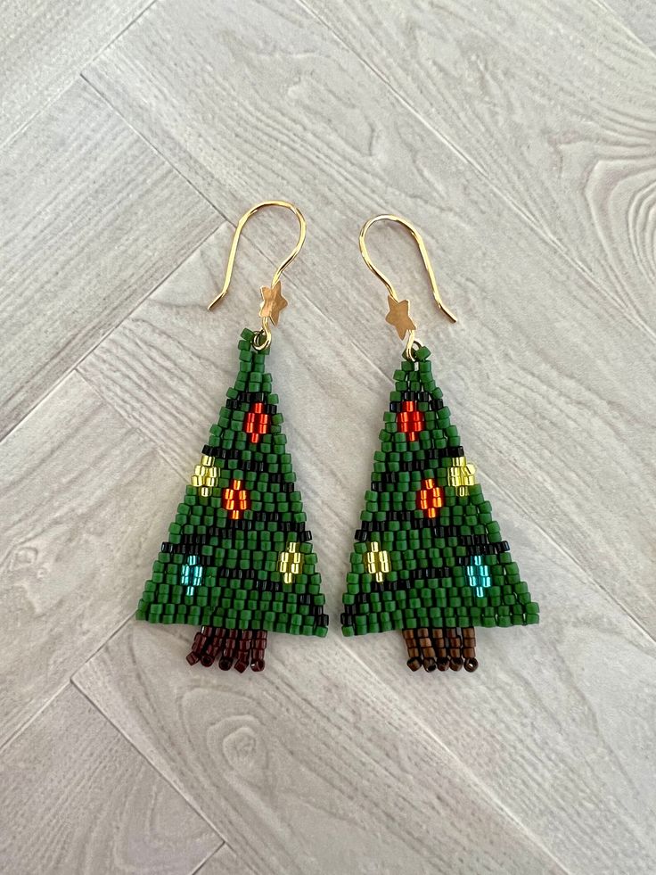 a pair of green beaded christmas tree earrings on wooden floor next to white wall