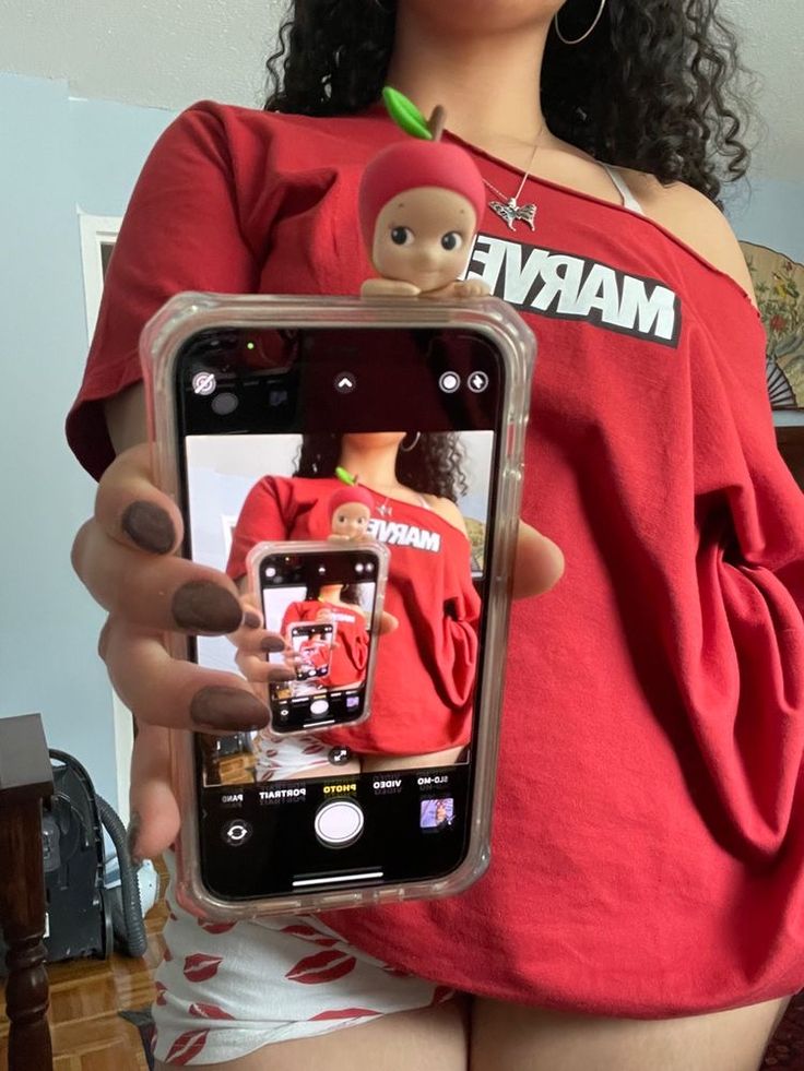 a woman holding up a cell phone with an image of a doll on the screen