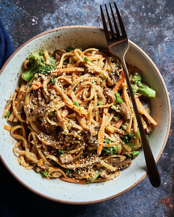 a white bowl filled with noodles and broccoli on top of a blue table