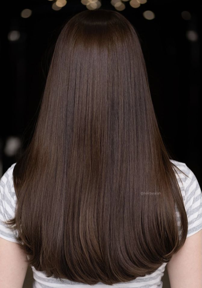 the back of a woman's head with long, straight brown hair and lights in the background