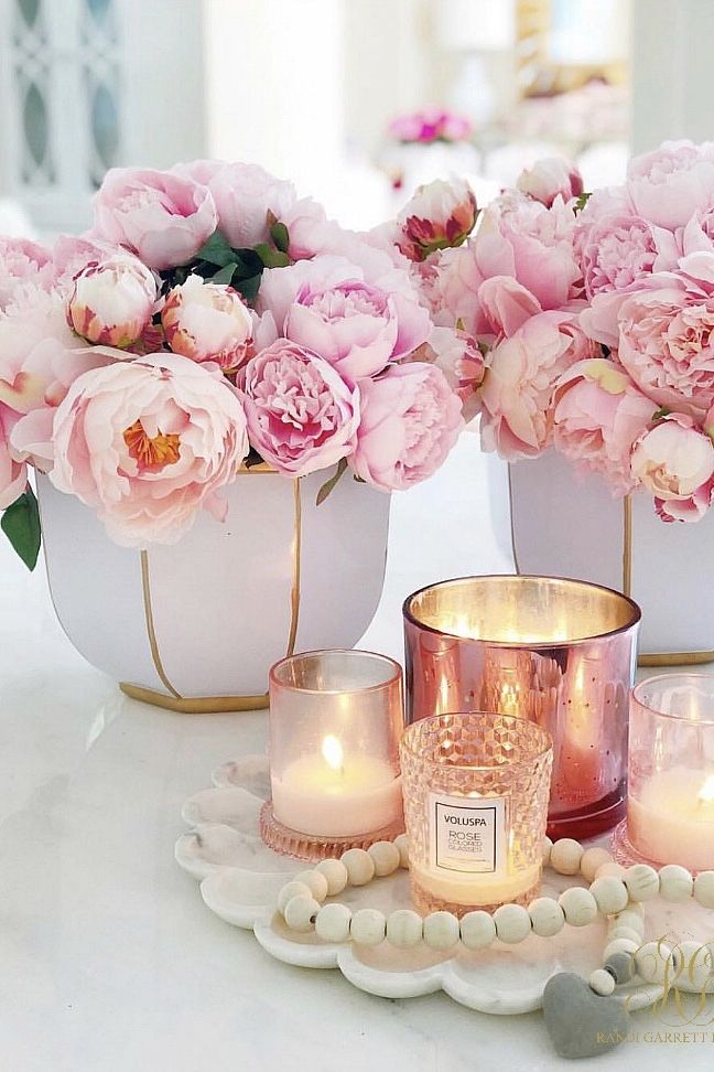 three vases filled with pink flowers sitting on top of a table next to candles