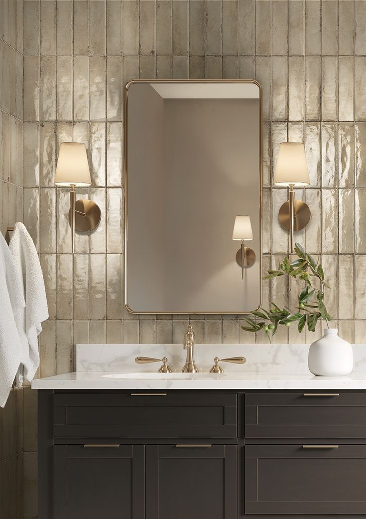 a bathroom vanity with two lamps and a large mirror above it, in front of a tiled wall