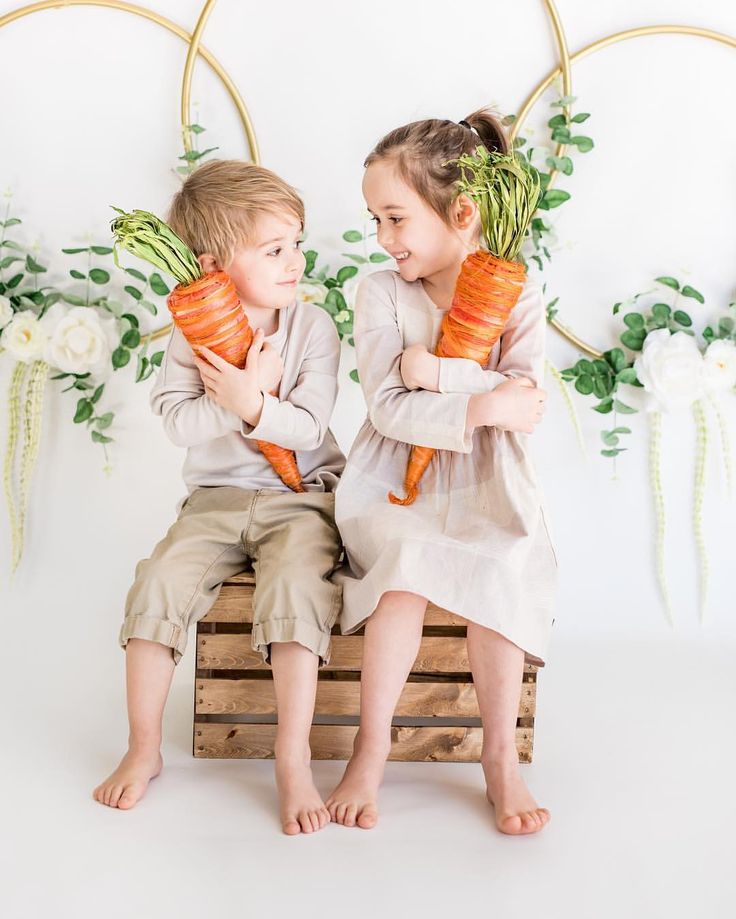 two children sitting on a crate holding carrots