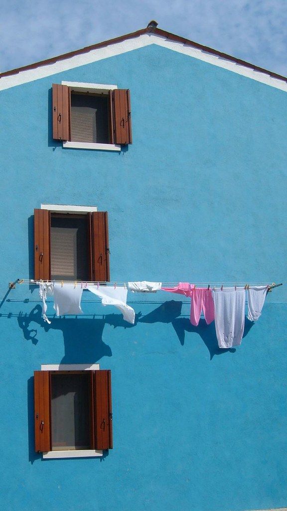 clothes hanging out to dry in front of a blue building with windows and shutters