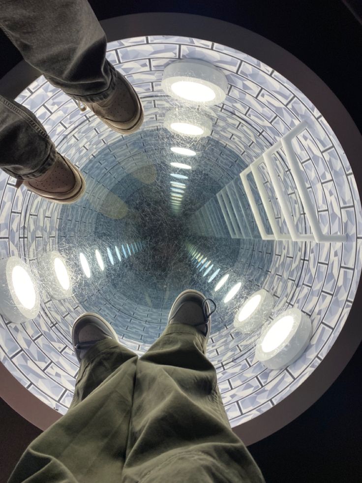 two people standing in front of a round glass window looking up at the sky from below