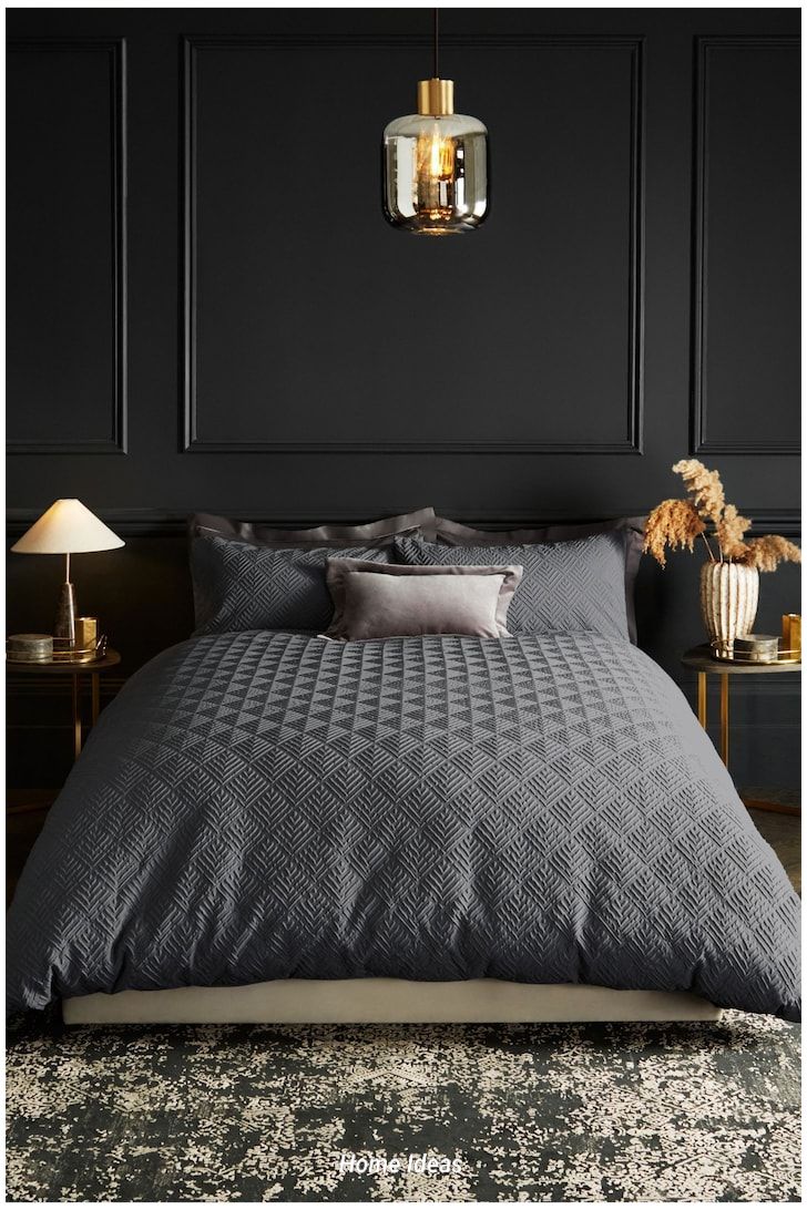 a bedroom with black walls and grey bedding, two lamps on either side of the bed