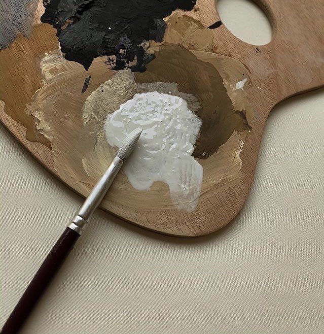 a wooden palette with some white and black paint on it next to a brown brush